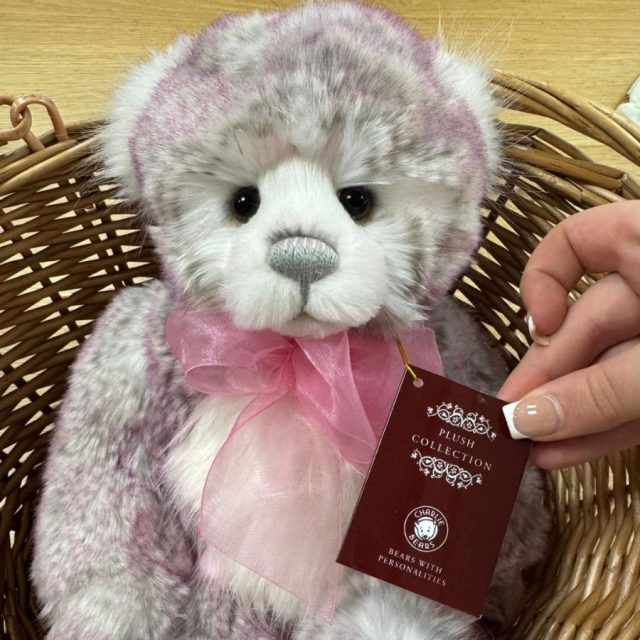 Amelie by Charlie Bears Close-up of Charlie Bears Amelie plush bear with pink ribbon and tag in basket