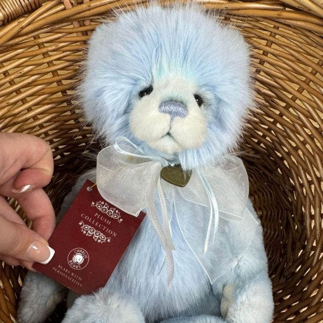Plus Collection Gaynor Close-up of Charlie Bears Gaynor plush bear holding a red Plush Collection tag